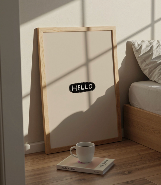 Framed artwork with 'HELLO' text on a wooden floor next to a book and mug.