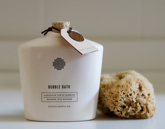 White bottle of bubble bath with a tag and a natural sponge on a light background