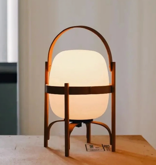 Table lamp with wooden frame and white glass shade on a wooden surface.